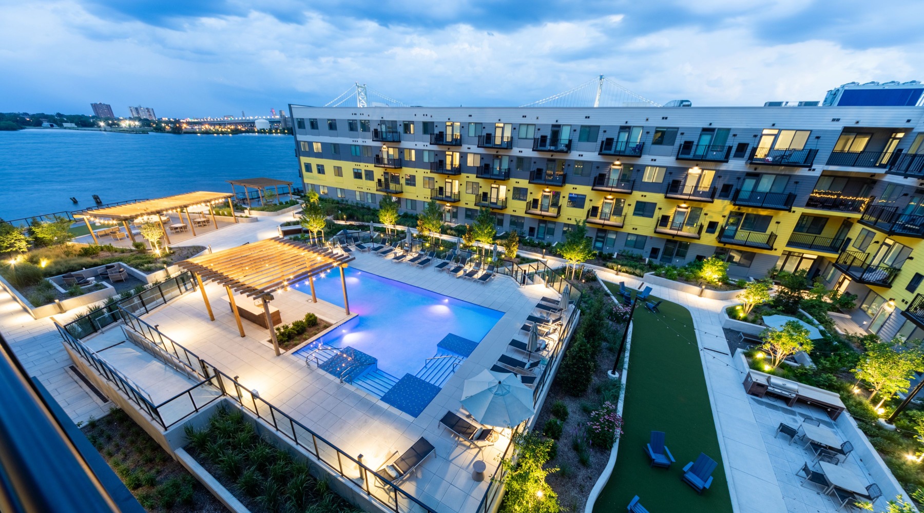 courtyard area aerial shot with grass, grills,  tables and chairs by building exteriorand water at at dusk Rivermark Northern Liberties Apartment in Philadelphia