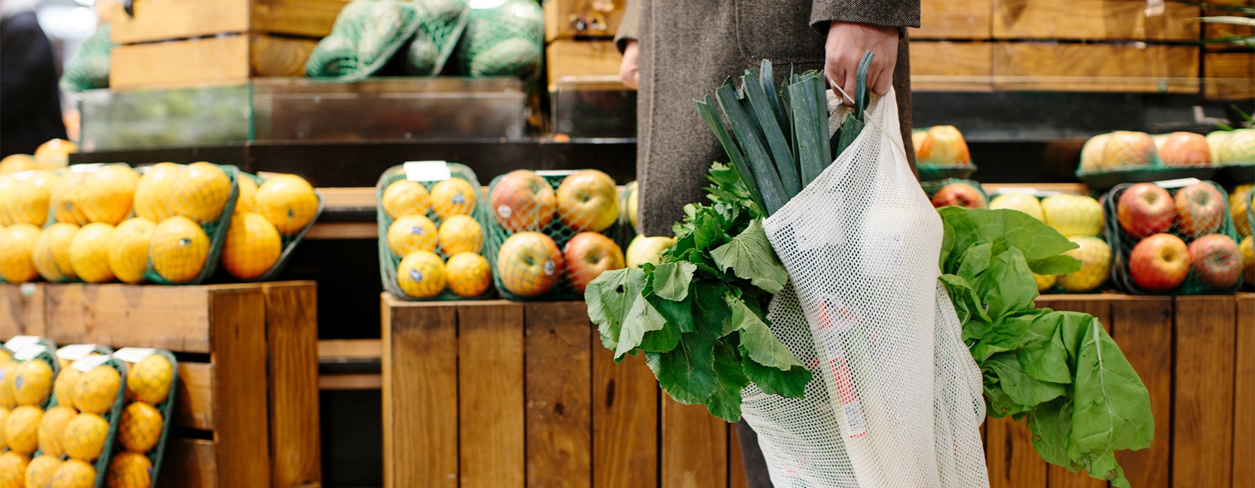 a man carrying a bag of produce in a produce section of a grocery store